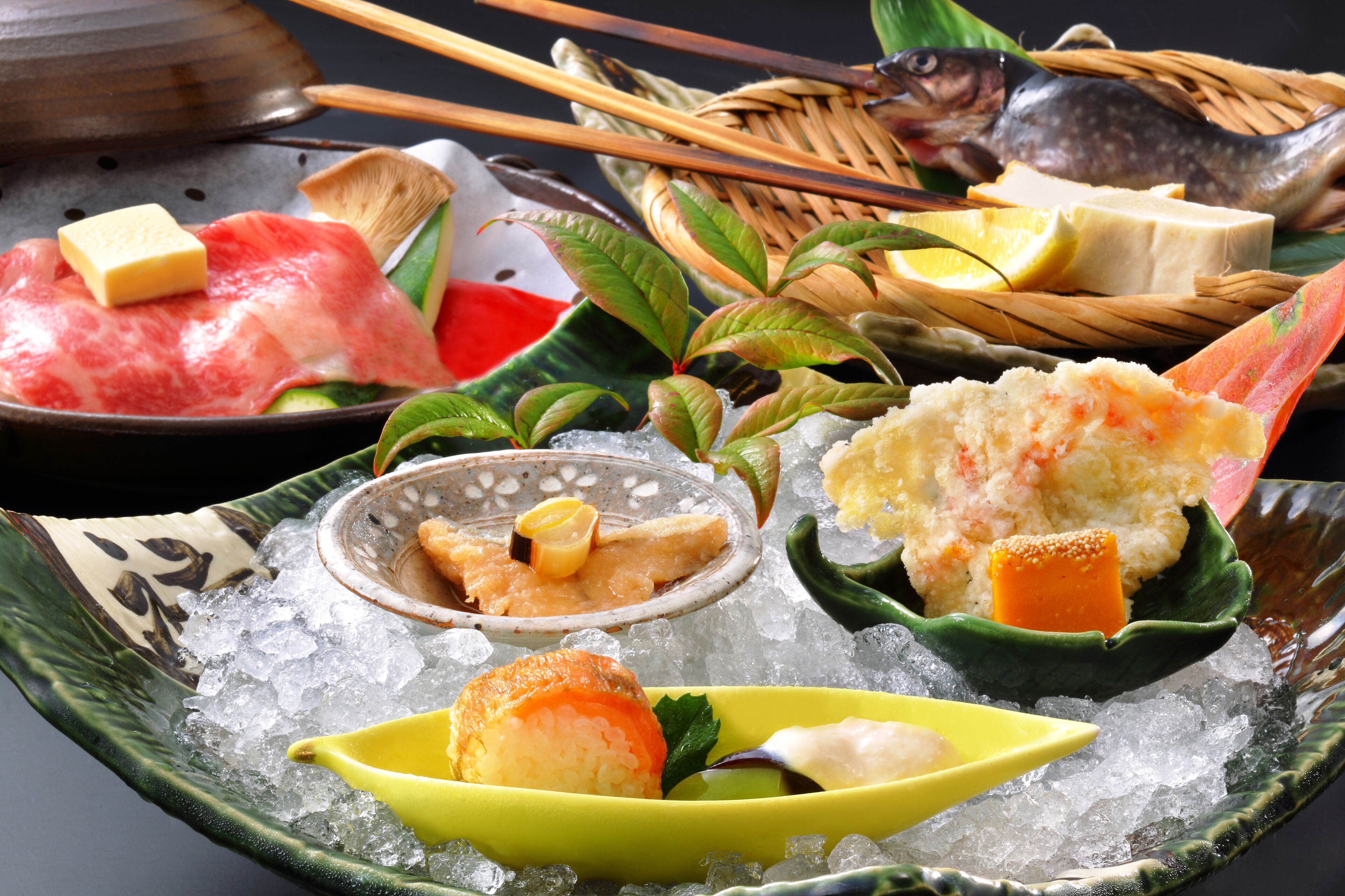A variety of sushi and sashimi on a bed of ice, accompanied by chopsticks, a fish, and a small bowl of sauce.