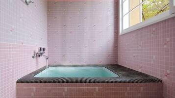 A bathroom with pink tiled walls, a bathtub, and a window with a view of trees.