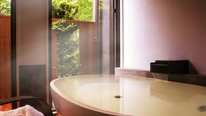 Un cuarto de spa con una bañera grande, una puerta de madera y una ventana con vistas a follaje.