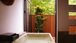 Un jacuzzi en una habitación con suelo de madera, valla de madera y vistas a la vegetación.