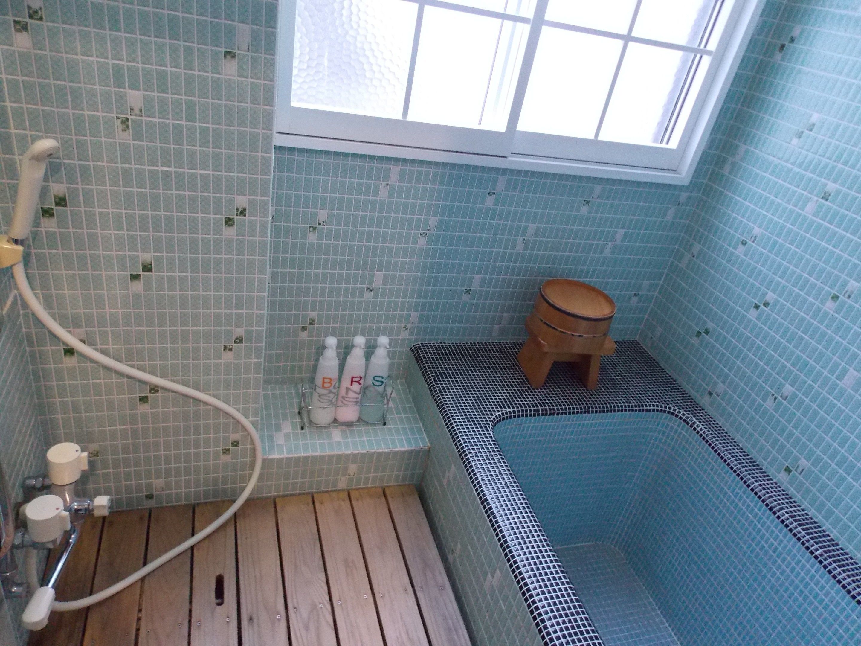 A bathroom with a bathtub, a wooden stool, and a rack holding bottles.