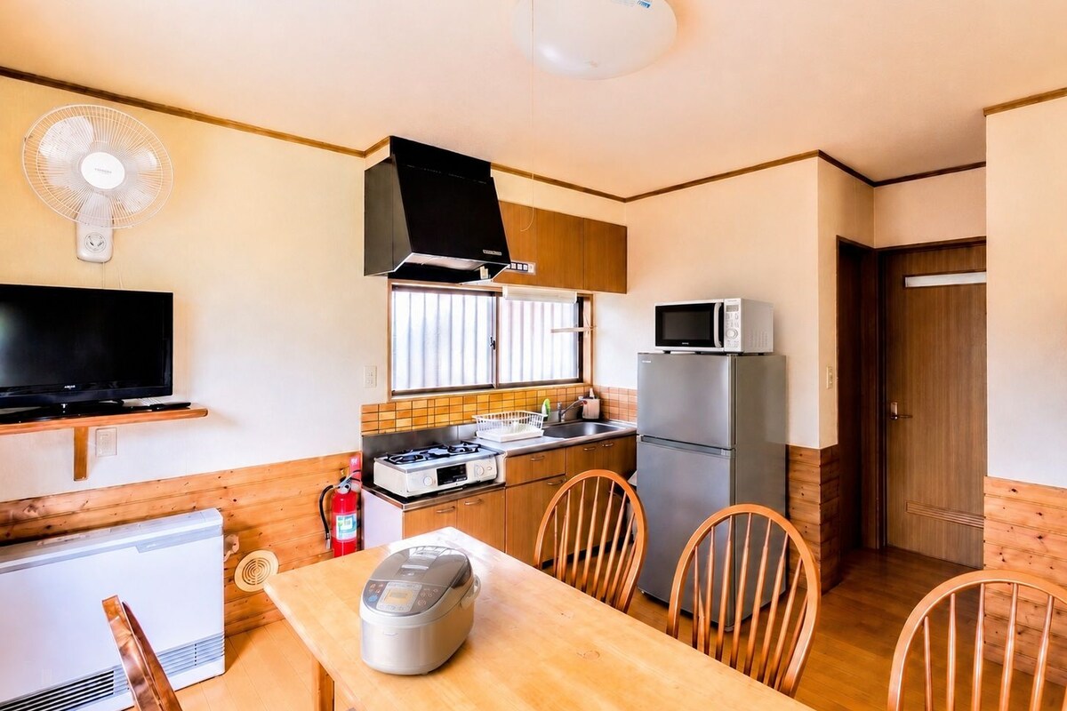 A compact kitchen with a stove, microwave, and refrigerator. There is a dining table with chairs and a television on a stand.