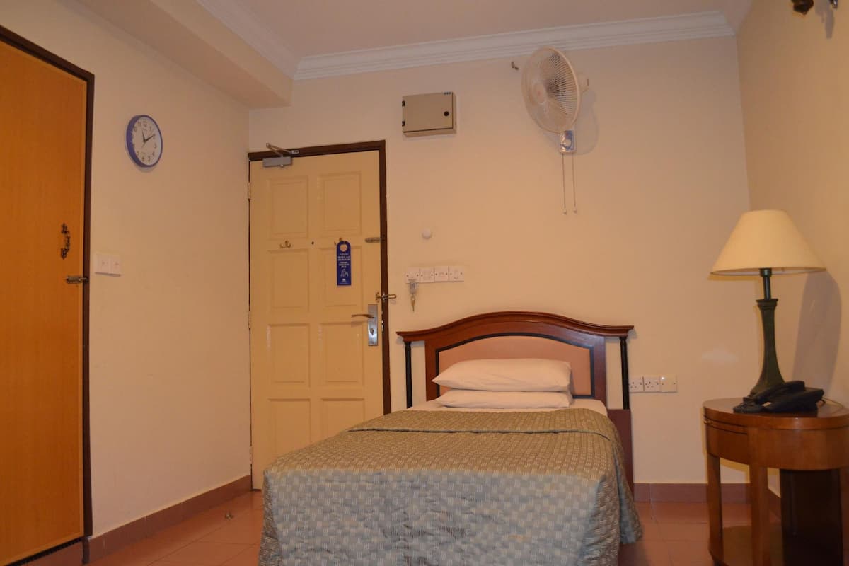 Une chambre d’hôtel avec un lit, une table de chevet avec une lampe, une horloge murale et un ventilateur de plafond.