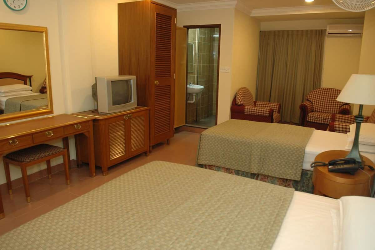 Une chambre d’hôtel avec deux lits, un bureau avec une télévision, un miroir et une salle de bain visible à travers une porte ouverte.