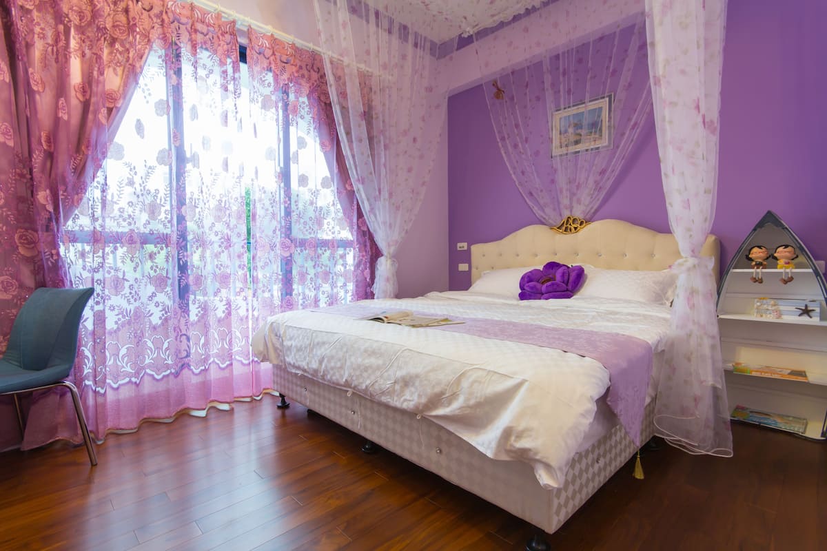 A bedroom with a bed, a chair, a bedside table, and a window with curtains.