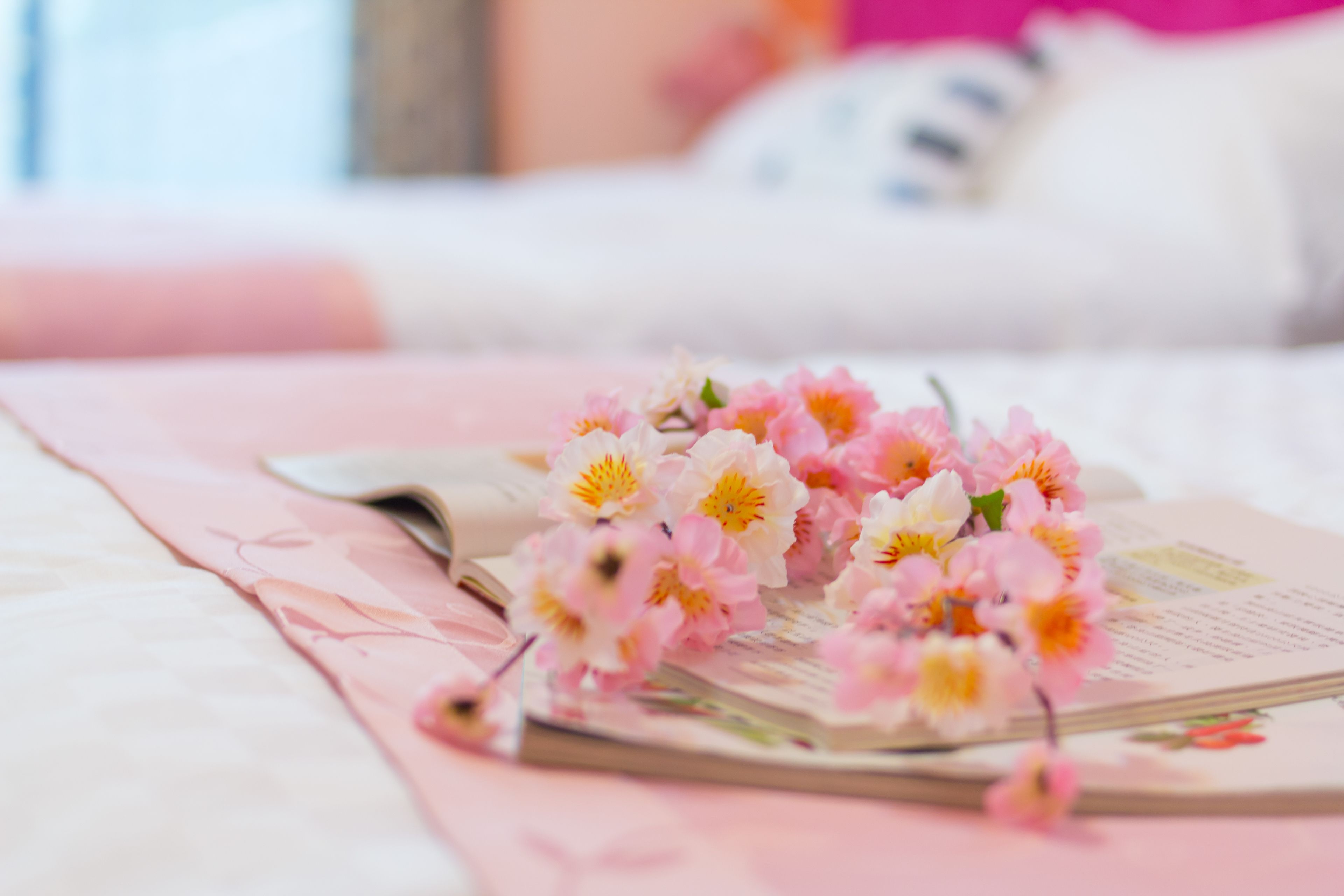A bed with a pink blanket and a book with flowers on it.