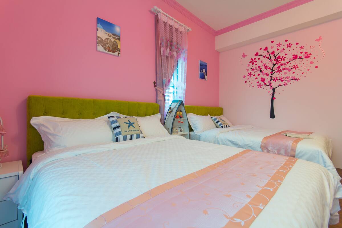 A room with two beds, a pink wall, and a tree mural.
