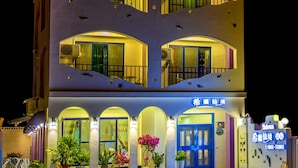 A multi-story hotel with balconies, a blue entrance, and potted plants.
