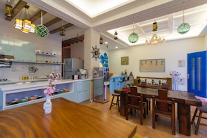 A modern kitchen with wooden cabinets, a dining area with a wooden table and chairs, and hanging pendant lights.