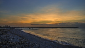 A coastal scene with a calm sea, a curved shoreline, and a distant lighthouse.