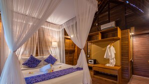 A bedroom with a canopy bed, wooden furniture, and a built-in shelf with a hanging garment. - Puri Pandawa Resort (Kutuh)