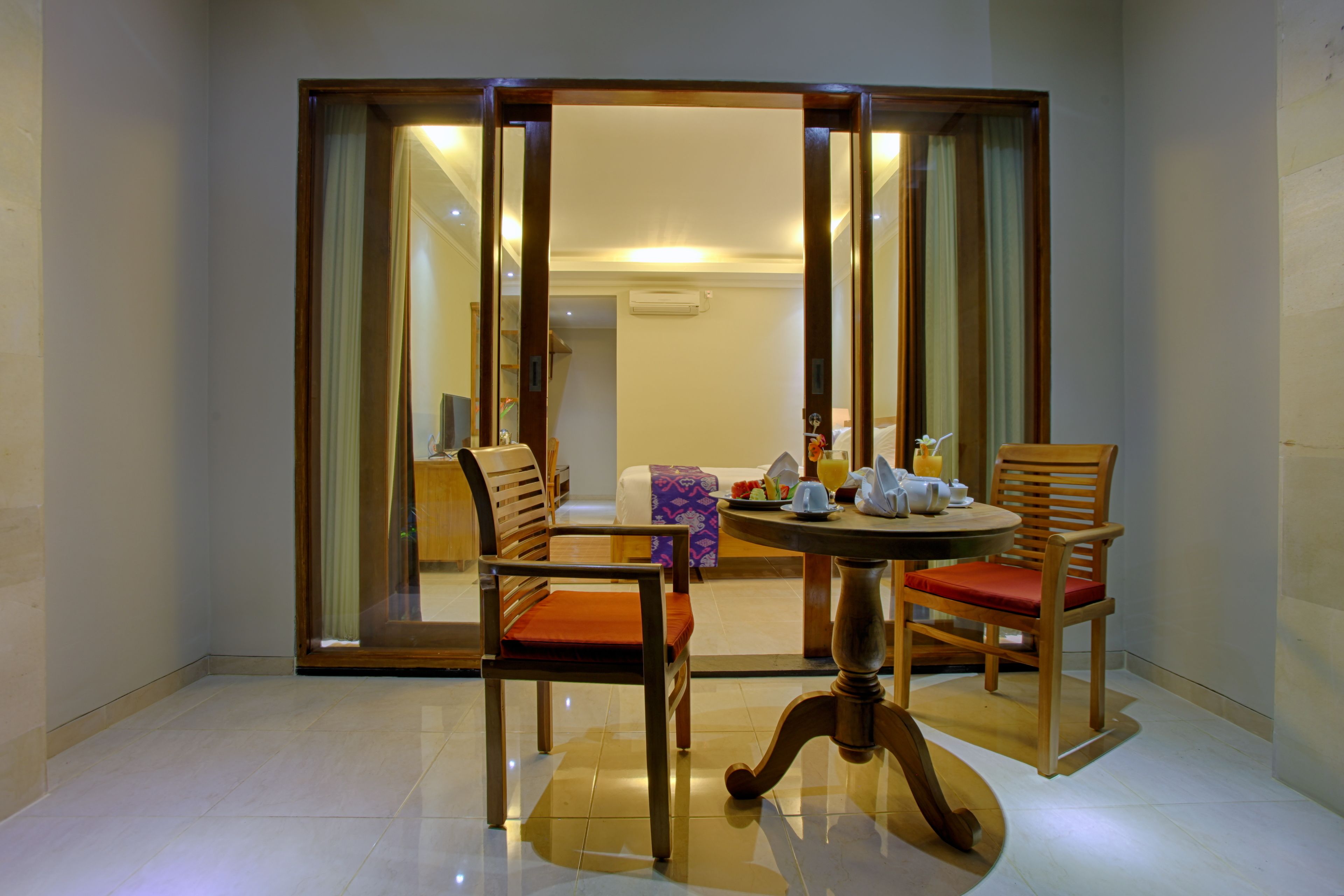 A dining area with a round table and two wooden chairs with red cushions, a wooden bench, and a glass partition.