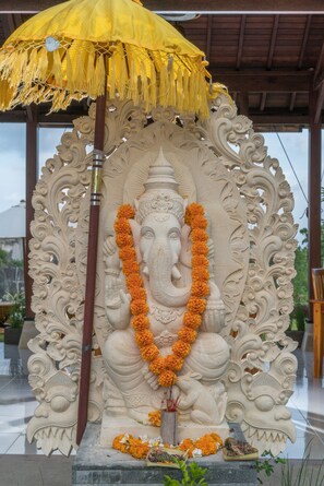 A statue of an elephant deity with intricate carvings, a yellow umbrella, and orange flowers. - Puri Pandawa Resort (Kutuh)