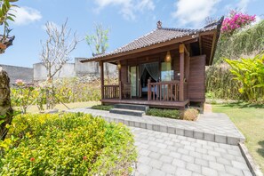A wooden house with a tiled roof, a porch, and a garden with various plants and flowers. - Puri Pandawa Resort (Kutuh)