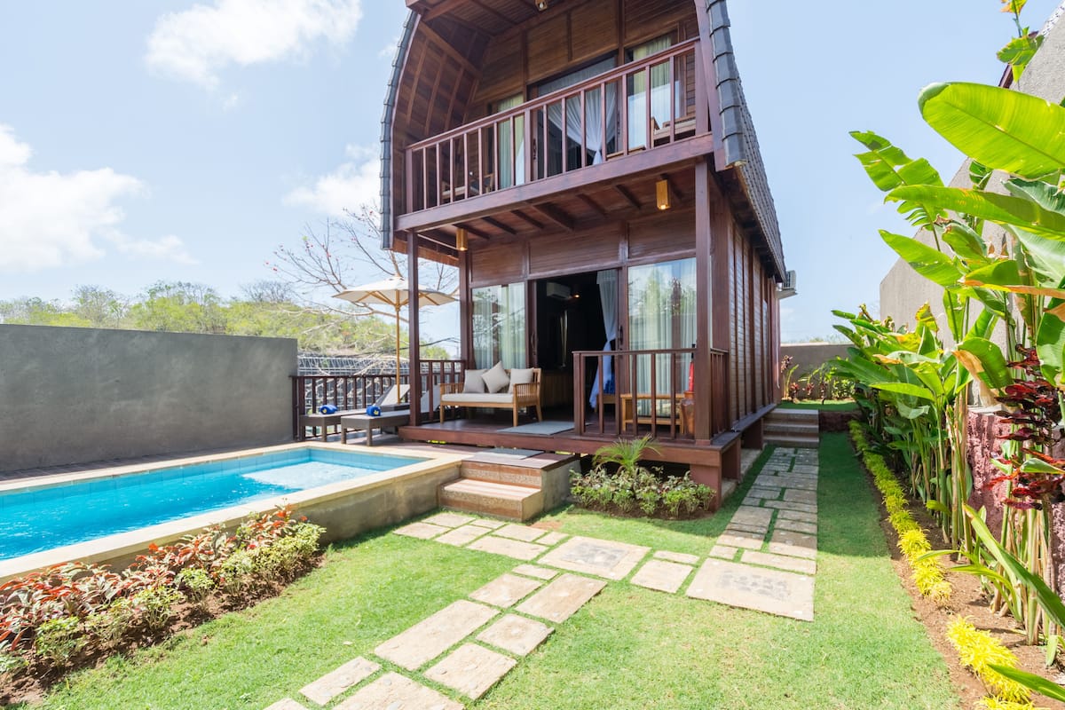A two-story wooden house with a balcony, a swimming pool, and a well-maintained garden.