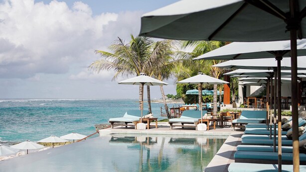 An infinity pool with lounge chairs and umbrellas, overlooking the ocean. - Puri Pandawa Resort (Kutuh)