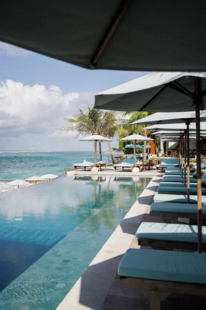 An infinity pool with lounge chairs and umbrellas, overlooking the ocean. - Puri Pandawa Resort (Kutuh)