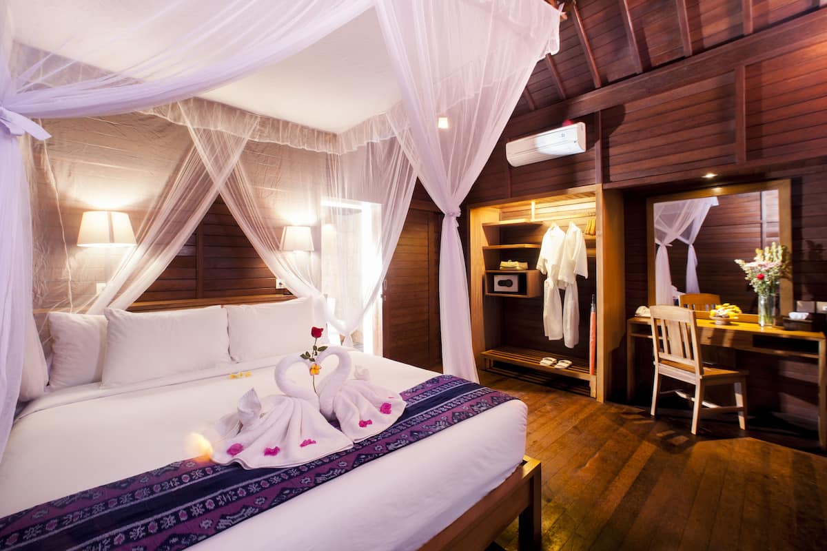 A well-appointed bedroom with a canopy bed, bedside lamps, a vanity with a mirror, and a wooden desk.