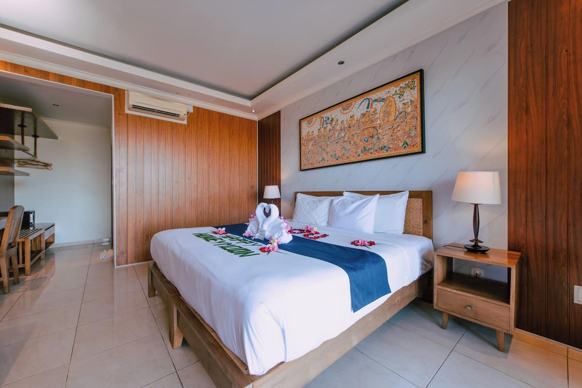 A hotel room with a bed, bedside table, lamp, and a wall with a large decorative piece.