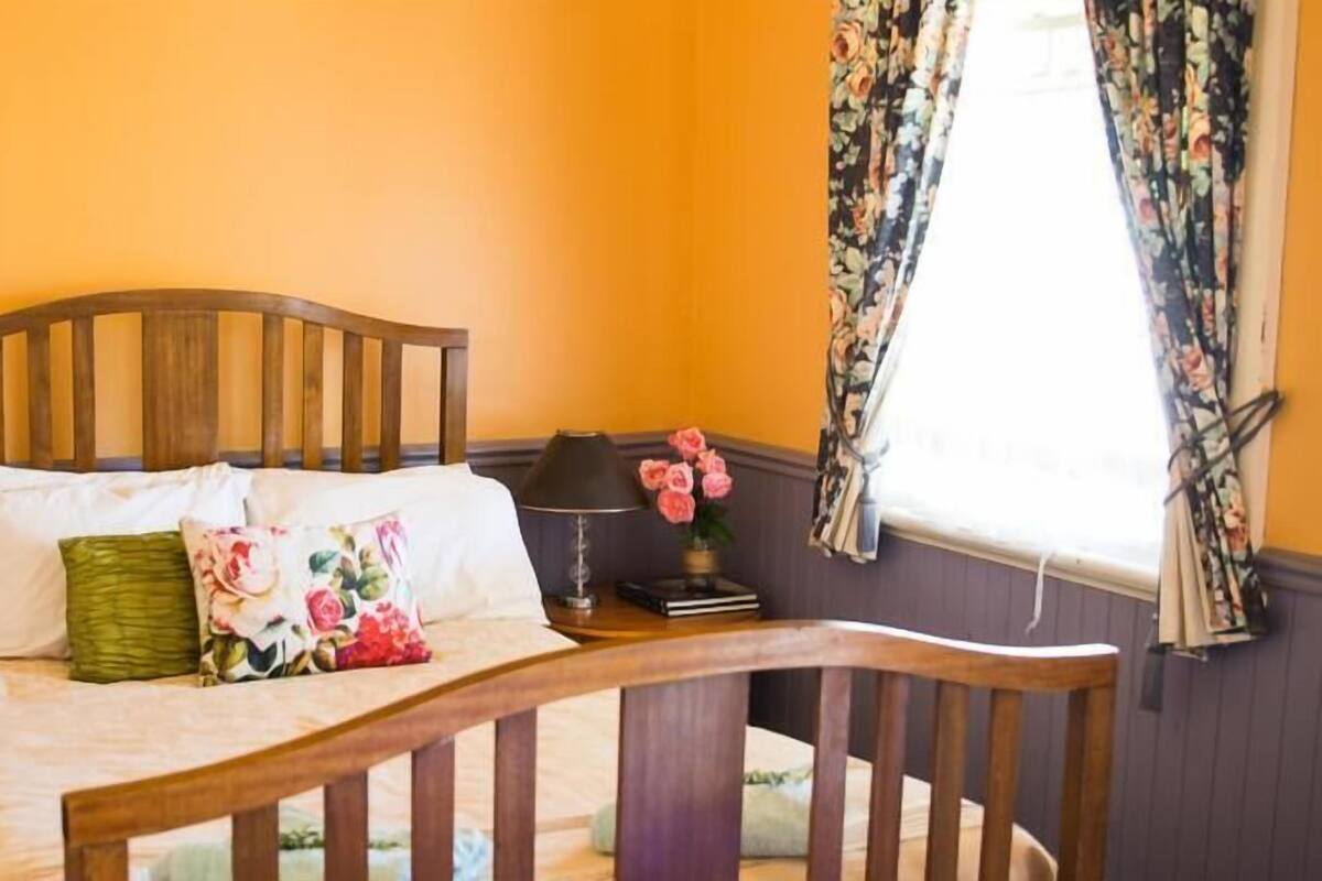Une chambre à coucher avec un lit en bois, une table de chevet avec une lampe et une fenêtre ornée de rideaux à motifs floraux.