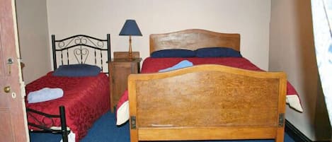 A bedroom with two beds, a wooden headboard, a nightstand with a lamp, and a framed picture on the wall.