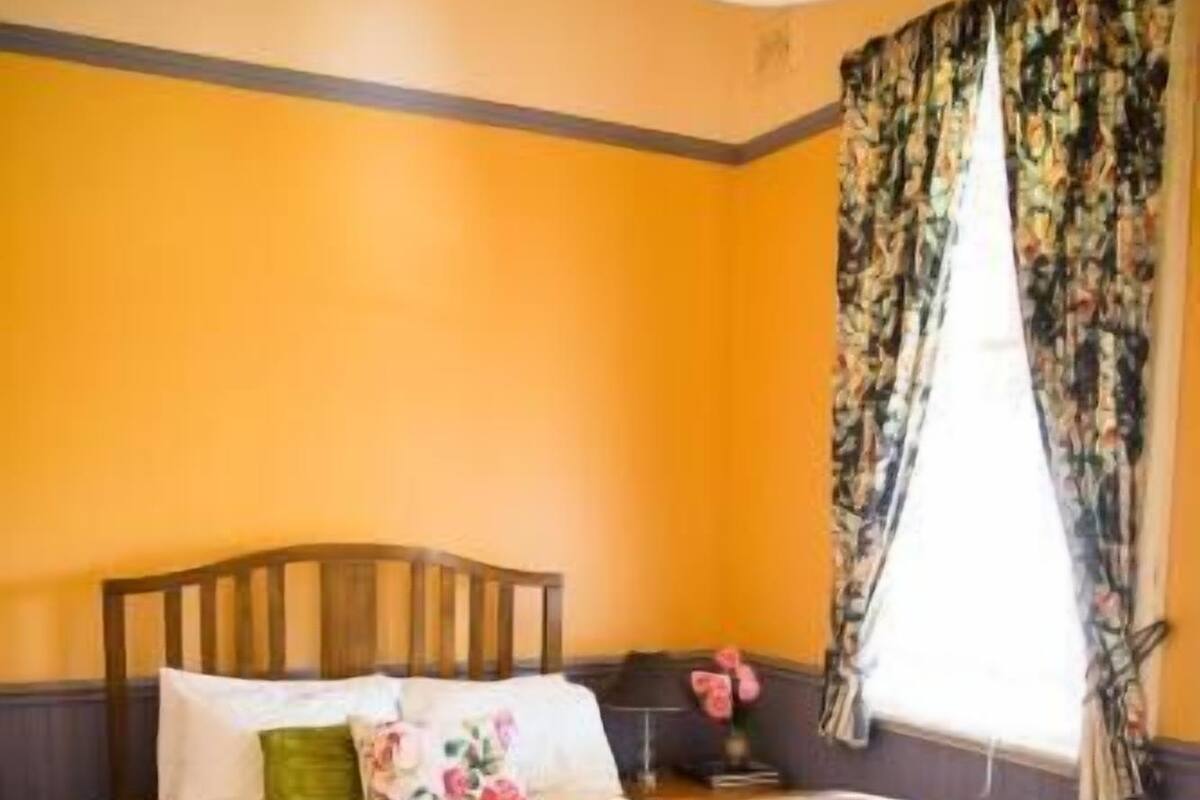 Une chambre avec un lit en bois, une table de chevet, une lampe et une fenêtre avec des rideaux.