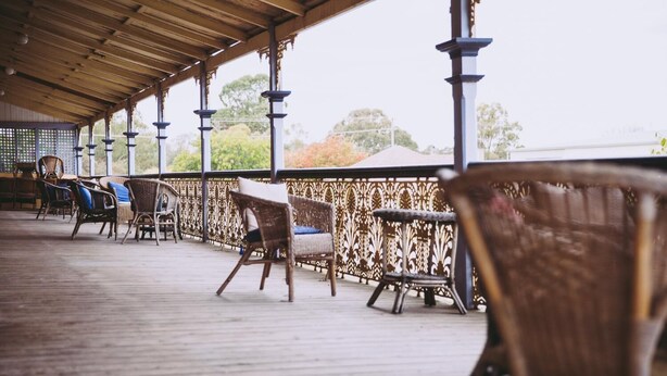 A covered outdoor seating area with wicker chairs and a wooden floor. - Boorowa Hotel (Boorowa)