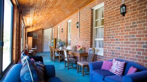 A cozy room with a wooden ceiling, brick walls, a dining table with chairs, and a blue sofa with a cushion. - Boorowa Hotel (Boorowa)