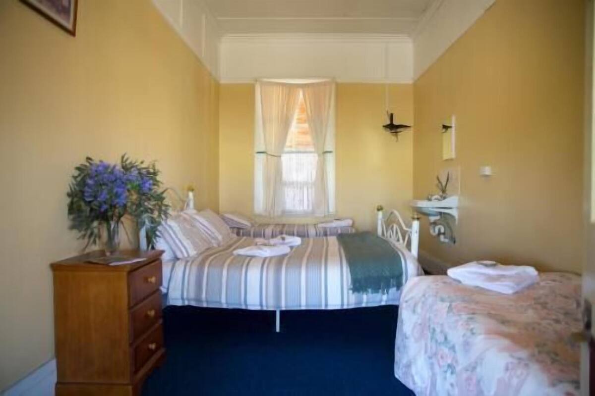 Une chambre à coucher avec un lit, une commode, une fenêtre avec des rideaux et une table de chevet.