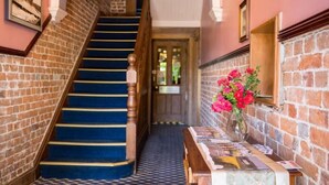 A staircase with blue carpet leading to a door, a brick wall, and a vase with red flowers on a table. - Boorowa Hotel (Boorowa)
