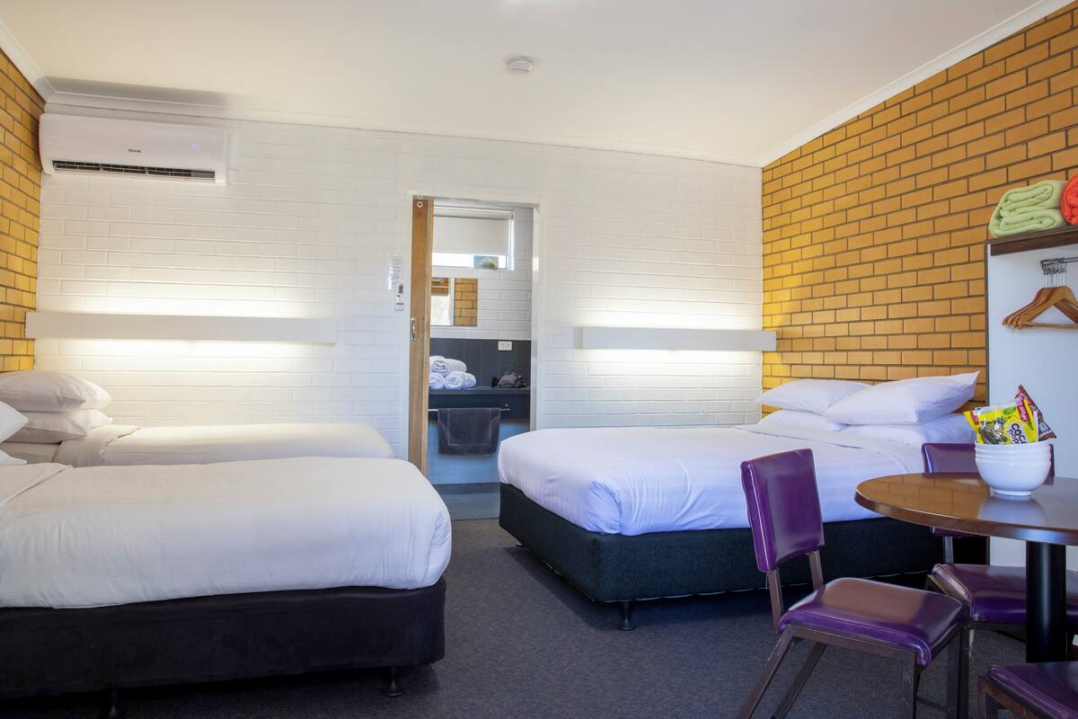 Ein Hotelzimmer mit zwei Betten, einem kleinen Tisch mit Stühlen, einer Wand mit Ziegelsteinen und einer weißen Klimaanlage.