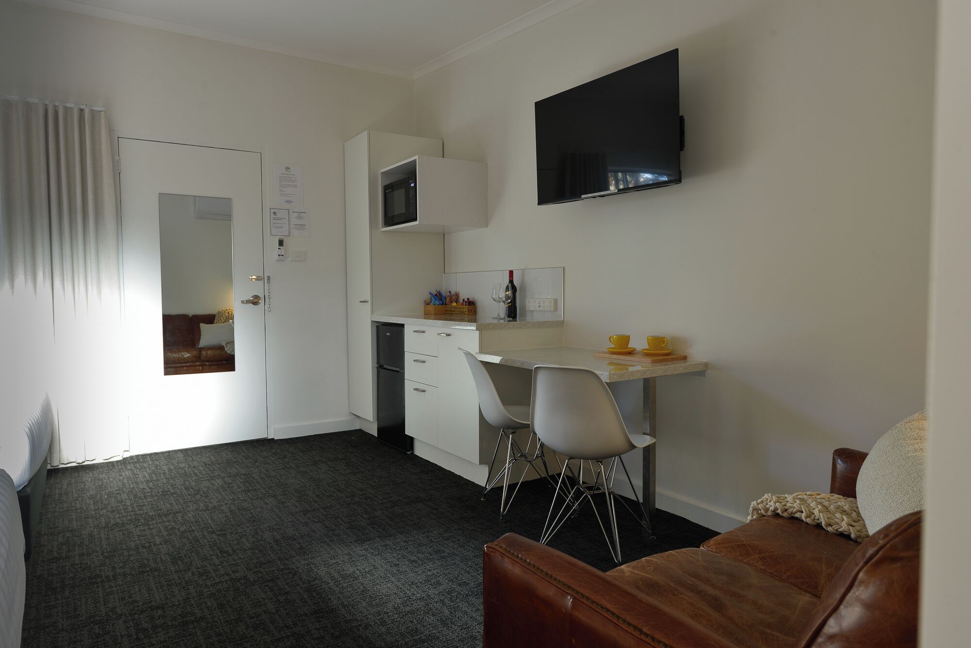 Een kleine kamer met een bed, een bureau met stoel, een televisie en een spiegel bij de deur.