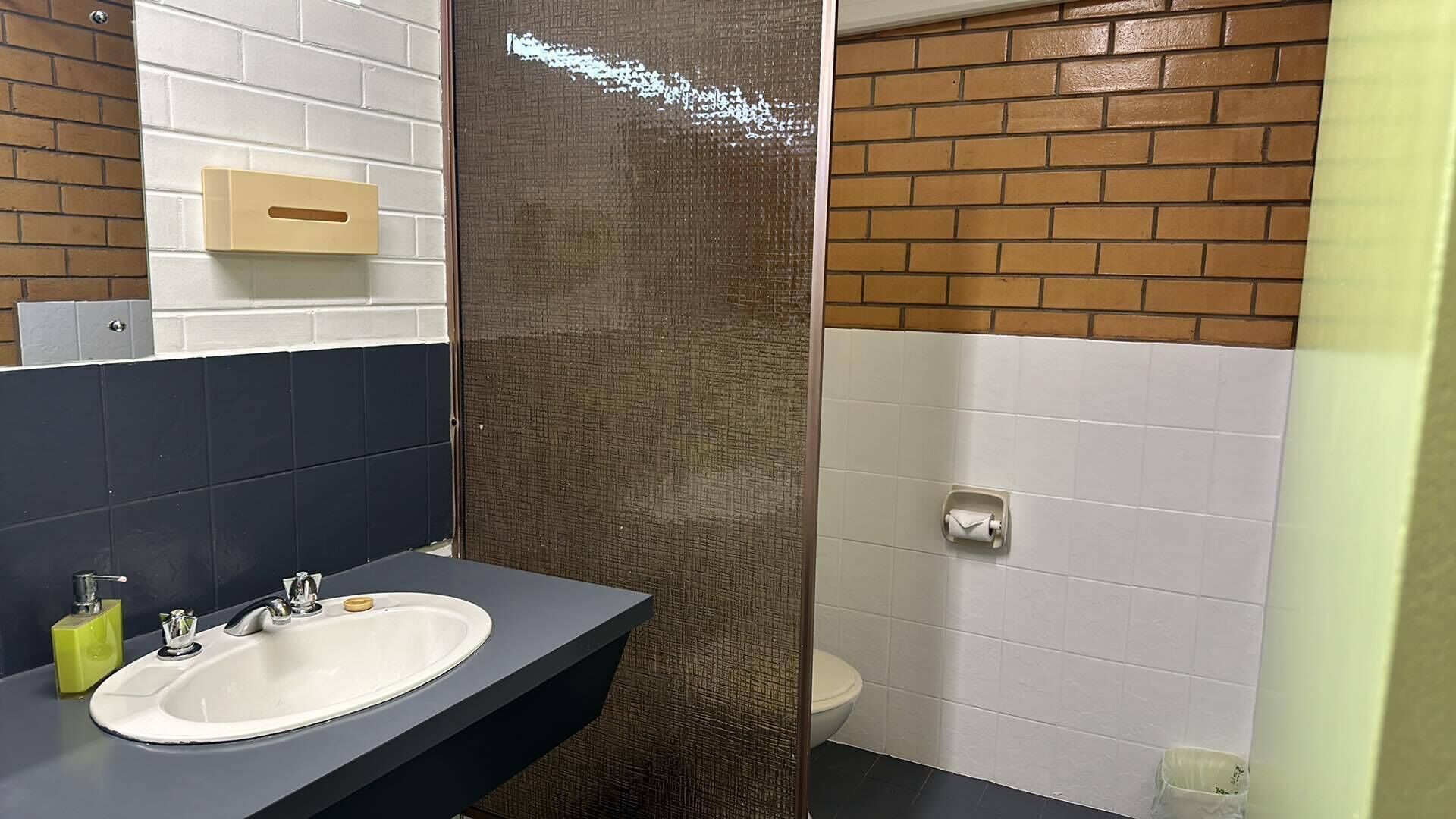 A bathroom with a white sink, dark blue countertop, and a shower area with a brown textured wall.