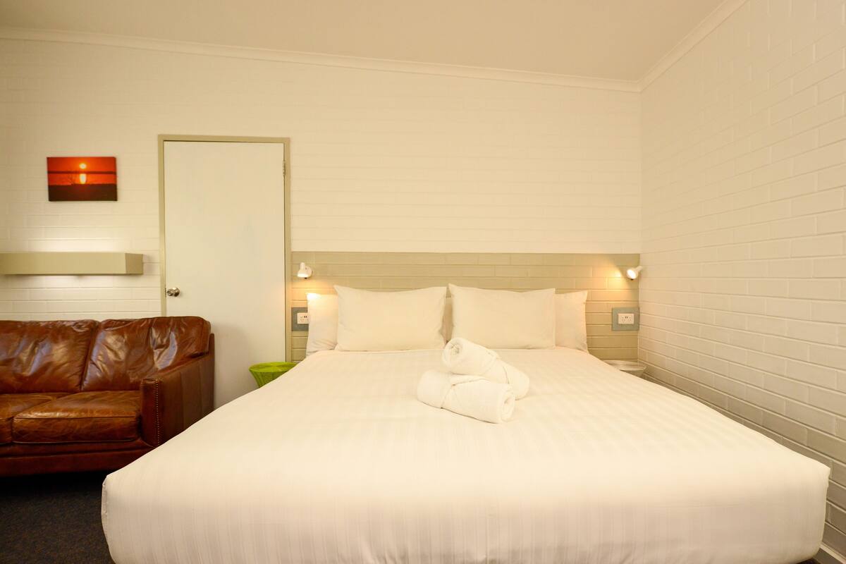 Ein Hotelzimmer mit einem großen Bett, einem braunen Ledersofa und einer Tür.