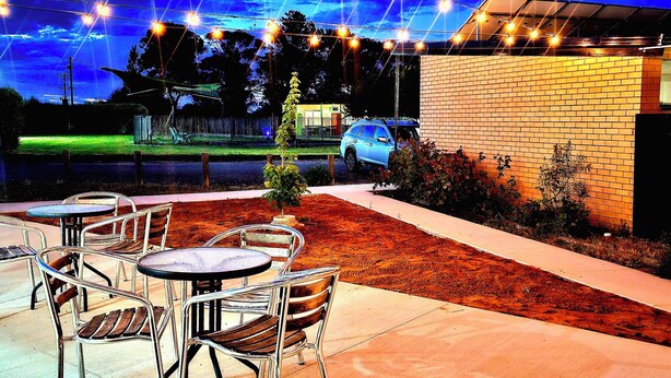 Un patio al aire libre con mesas y sillas, un muro de ladrillo y un coche estacionado al fondo.