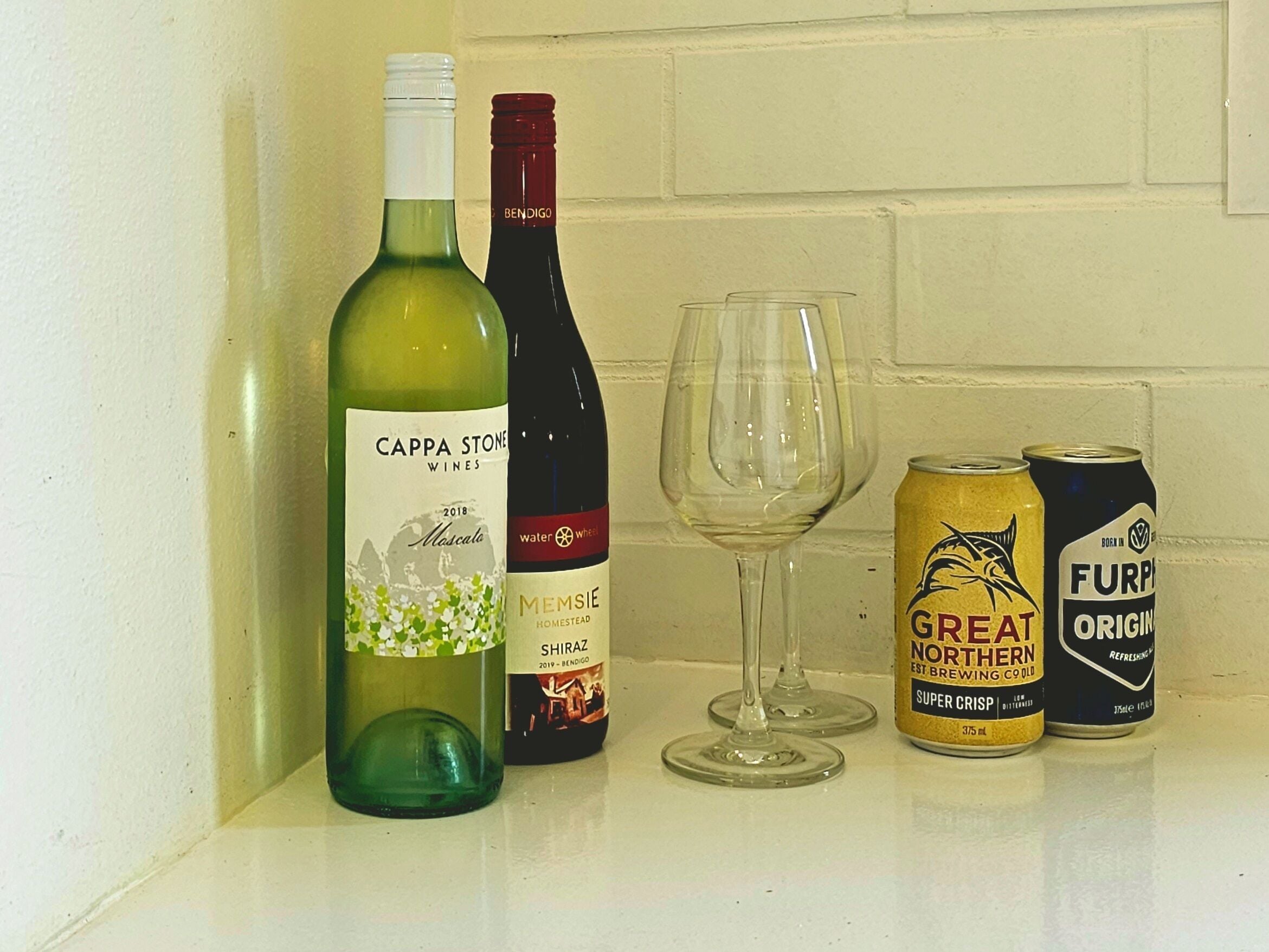 Twee flessen wijn, een wijnglas en twee blikjes bier op een toonbank.