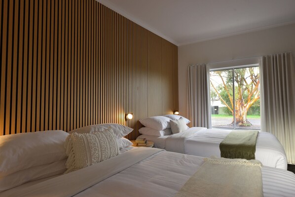 A hotel room with two beds, a wooden slat wall, a window with curtains, and a view of trees. - Sea Lake Motel (Sea Lake)