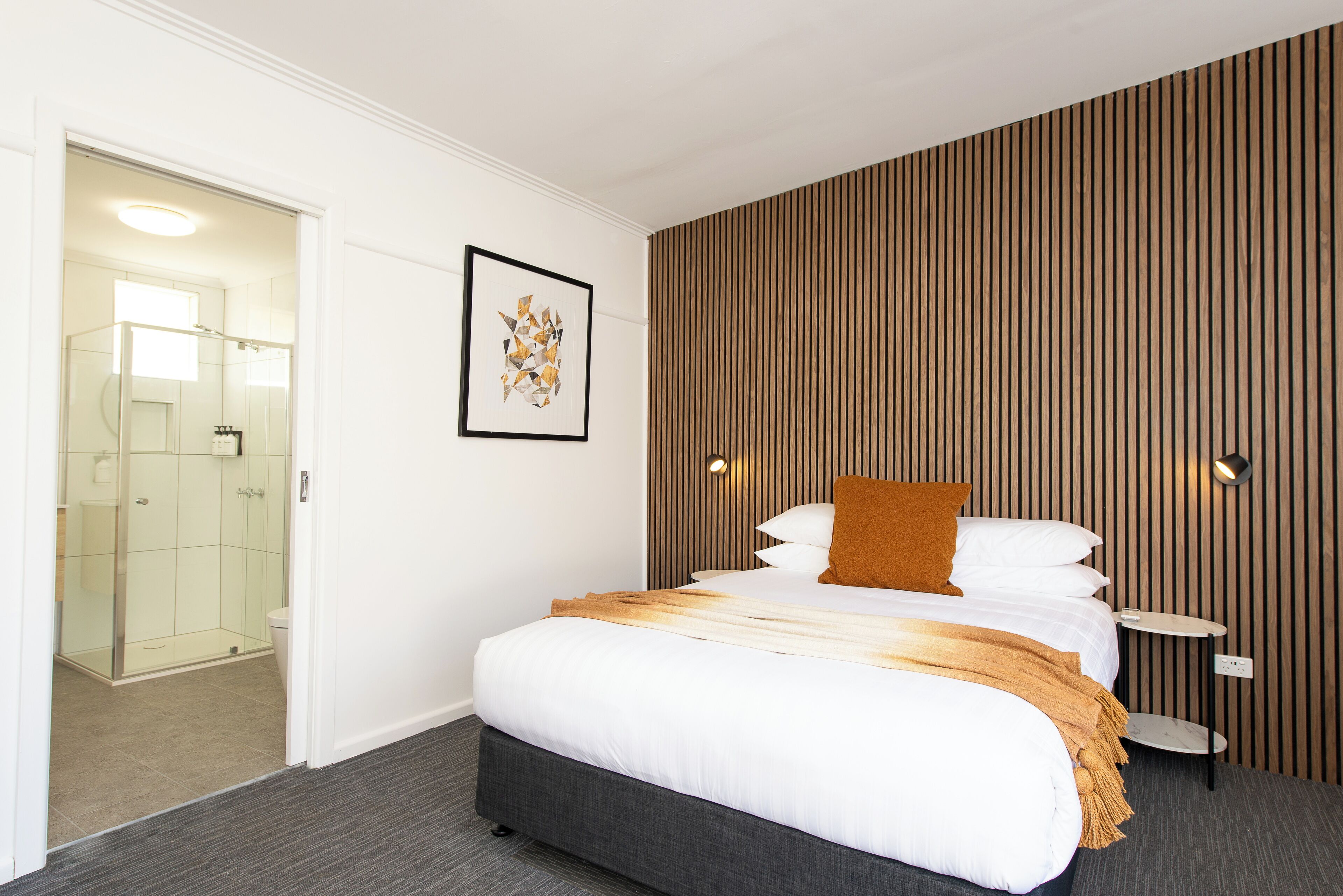 A hotel room with a large bed, a bedside table, a framed picture on the wall, and a wooden panel wall.