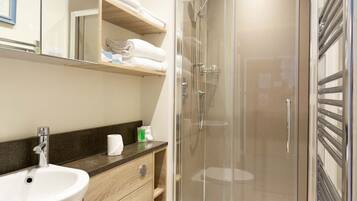 Un baño moderno con lavamanos, espejo, inodoro y ducha envuelta en vidrio.