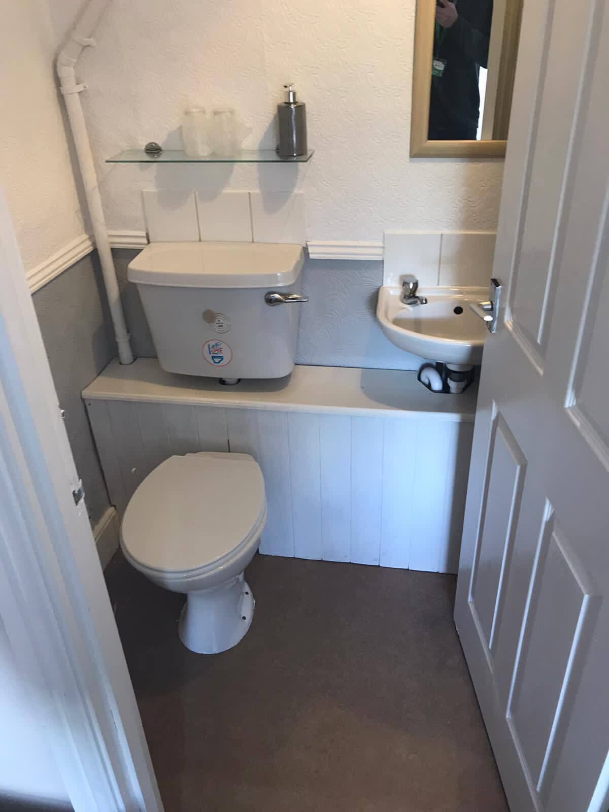 A compact bathroom with a toilet, a sink, and a shelf above the toilet.
