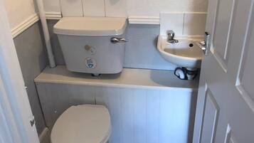 A compact bathroom with a toilet, a sink, and a shelf above the toilet.