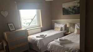 Une chambre d’hôtel avec deux lits simples, une commode en bois, une table de chevet avec une lampe et un tableau encadré posé sur la commode.