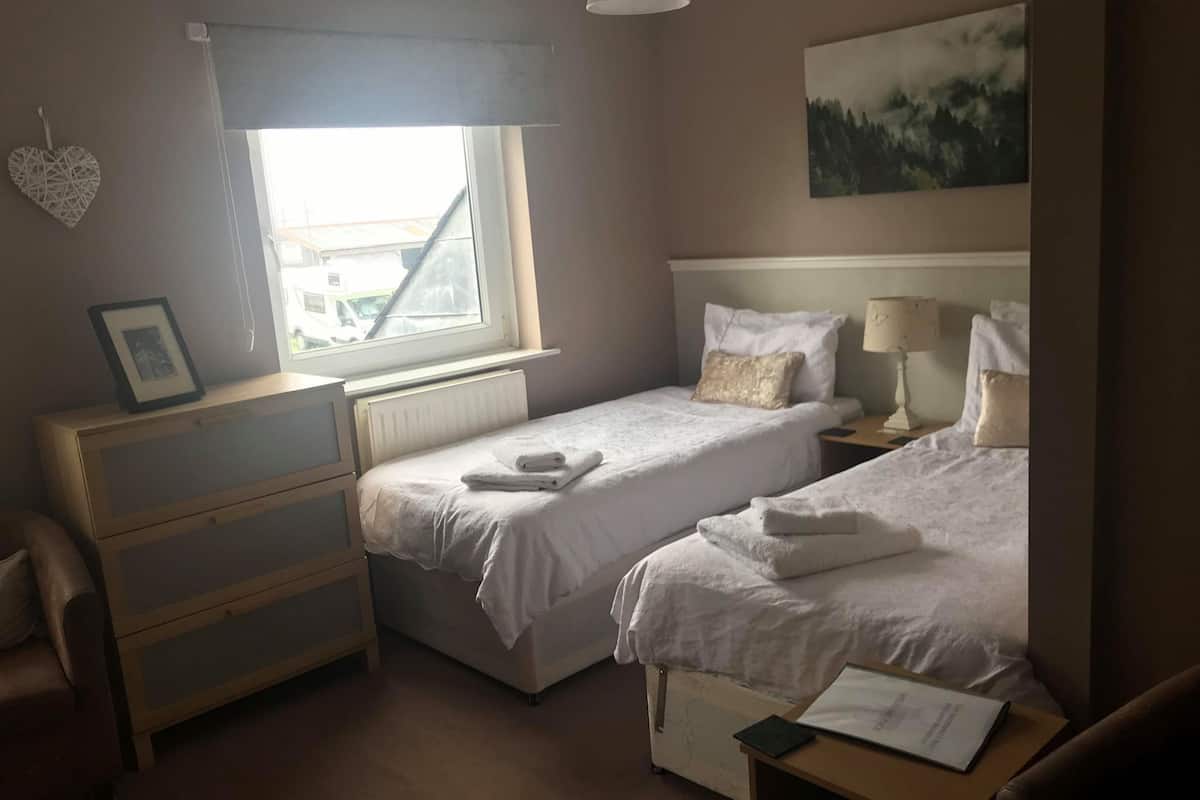 A hotel room with two single beds, a wooden dresser, a nightstand with a lamp, and a framed picture on the dresser.