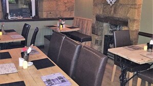 Un restaurant avec des tables en bois, des banquettes en cuir, des murs en pierre et une cheminée.