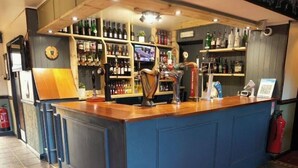 Un espace bar avec un comptoir bleu, des étagères remplies de bouteilles, une horloge et un extincteur.