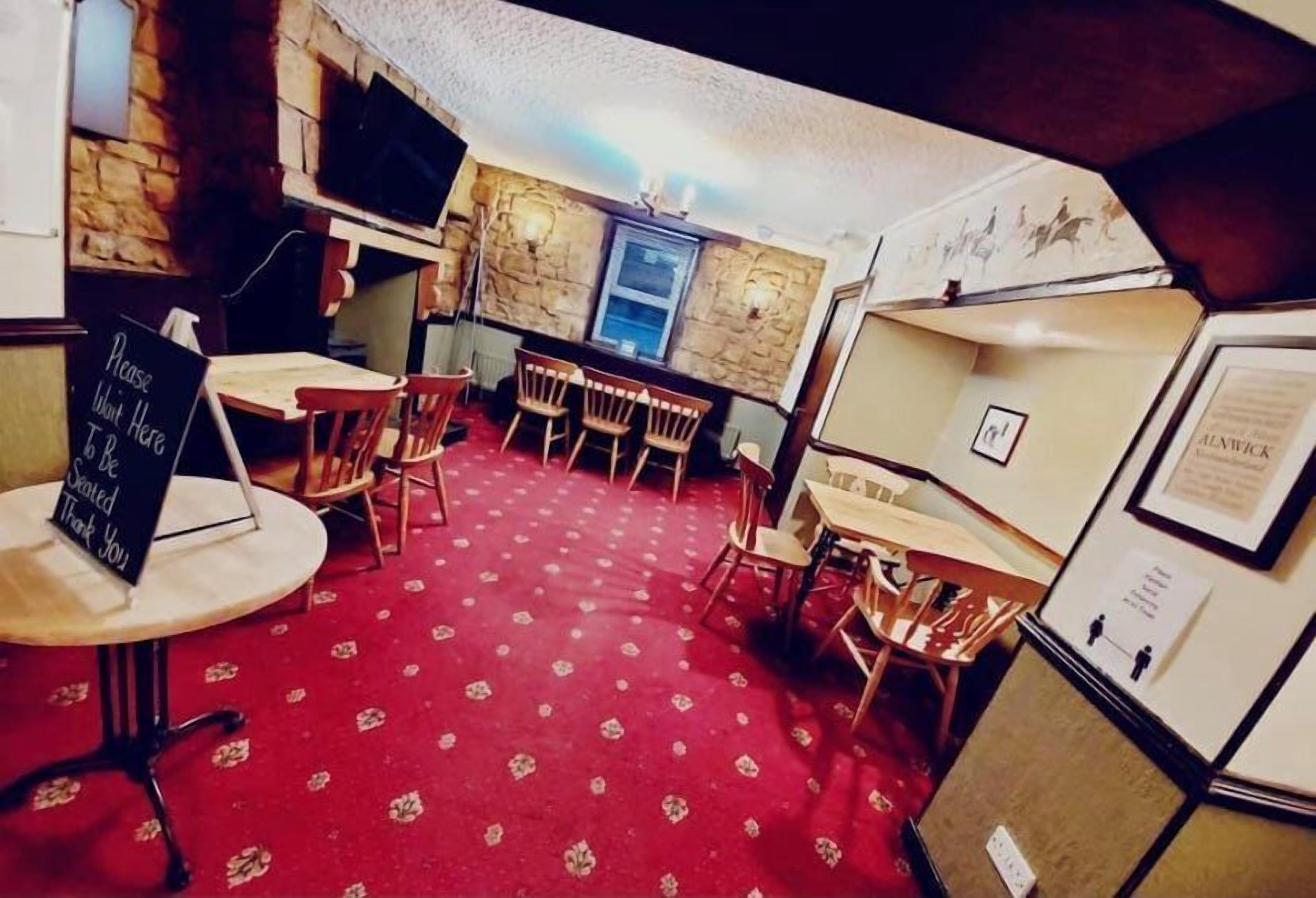 A cozy restaurant with a red carpet, wooden chairs, and a chalkboard sign.
