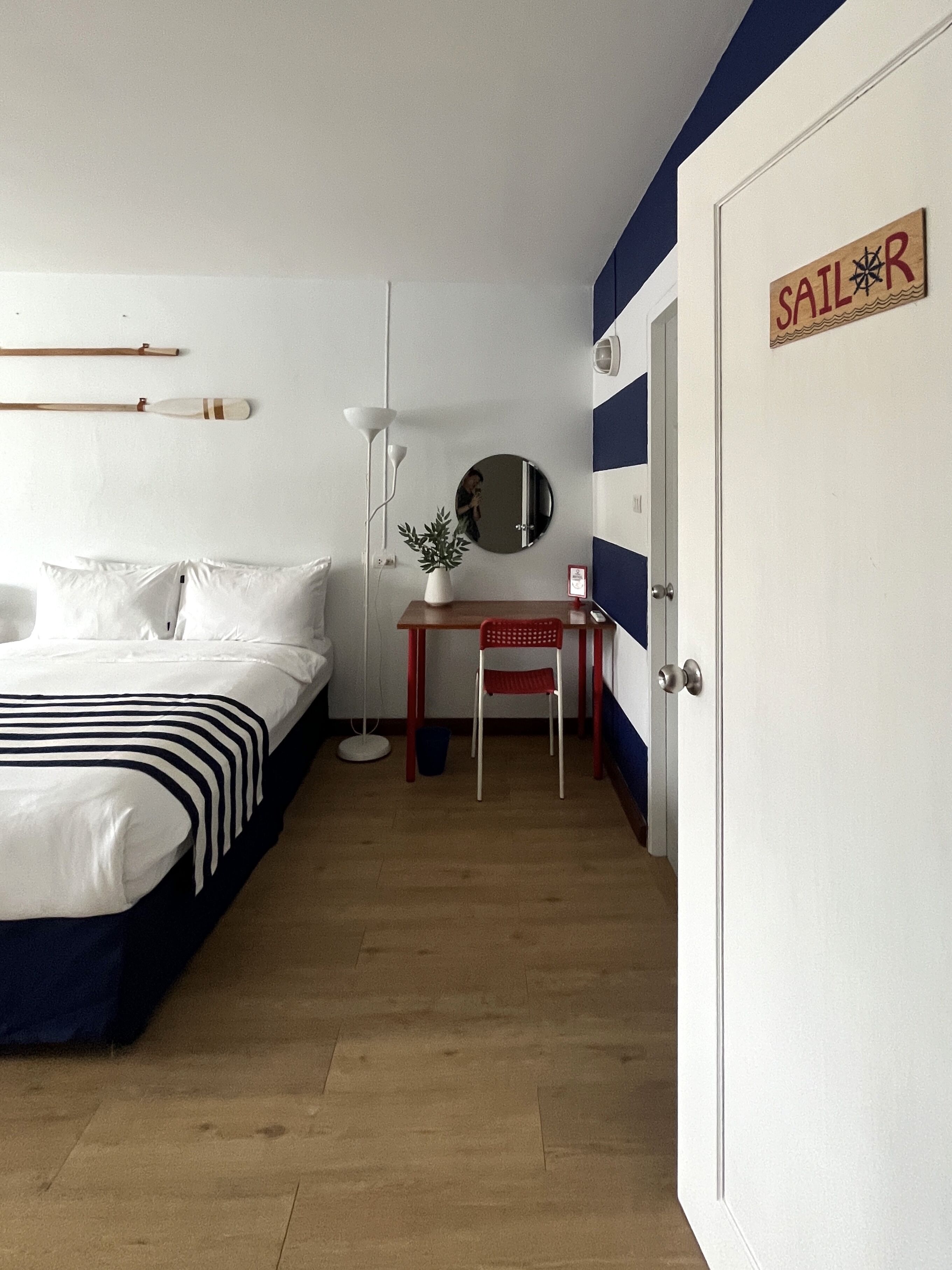 Un dormitorio con cama, escritorio, silla, espejo y puerta con un cartel.