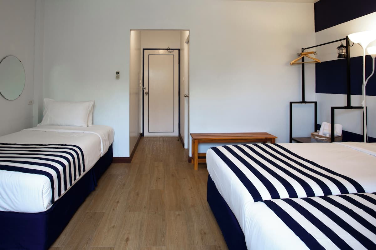 Una habitación de hotel con dos camas, suelo de madera, una mesita de noche, una lámpara colgante y una puerta.