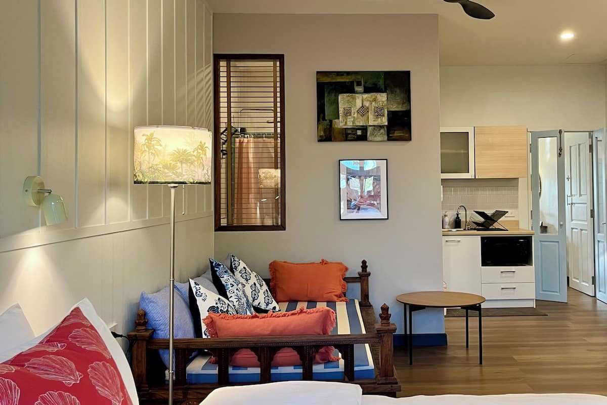 Una habitación con cama, lámpara de noche, ventana con cortinas, una obra de arte en la pared y ventilador de techo.