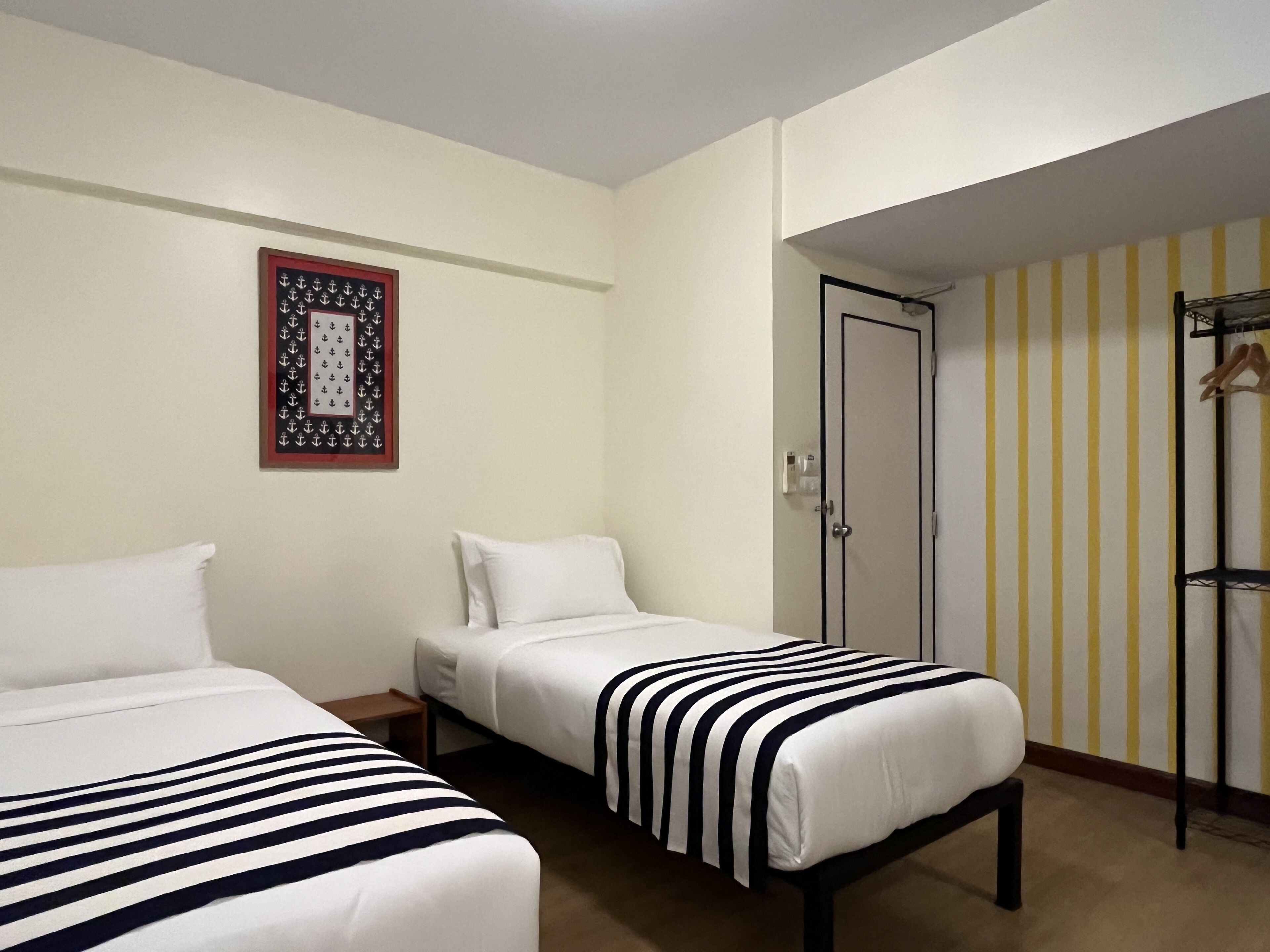 A hotel room with two beds, a framed picture on the wall, a door with a striped wallpaper, and a coat rack.